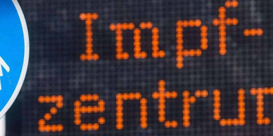 Eine elektronische Anzeigetafel mit dem Wort «Impfzentrum» hinter einem Verkehrsschild «Sonderweg Fussgänger» weist den Weg zu einem Impfzentrum. Foto: Julian Stratenschulte/dpa