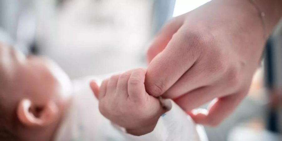 Ein Baby klammert sich an einen Finger seiner Mutter. (Archivbild). Foto: Fabian Strauch/dpa