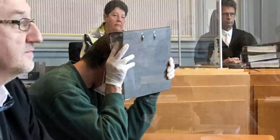 Der Angeklagte versteckt sein Gesicht im Gericht hinter einem Aktenordner. Foto: Karen Katzke/dpa