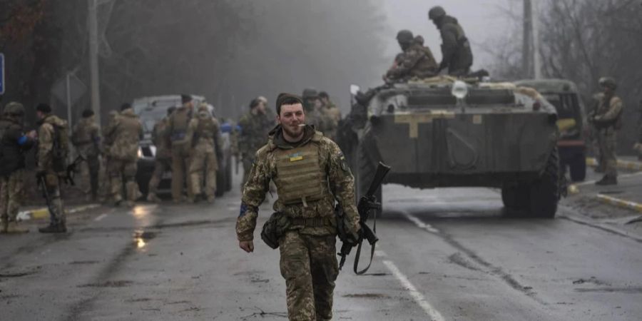 Ukrainische Soldaten im Ukraine-Krieg in Vollmontur, begleitet von einem Panzerwagen.