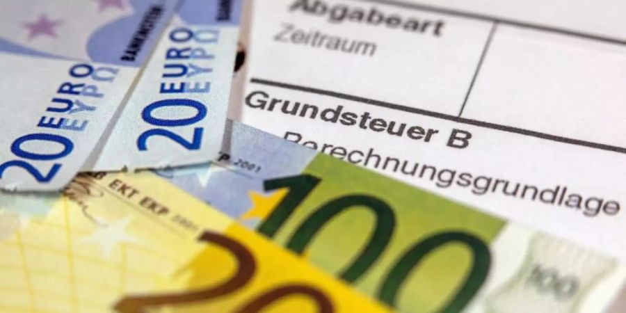 Euro-Geldscheinen liegen auf einem Abgabenbescheid für die Entrichtung der Grundsteuer. Foto: Jens Büttner/Archivbild