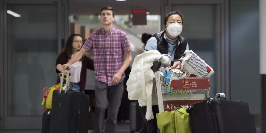 Eine Frau trägt am Toronto Pearson International Airport eine Atemschutz-Maske. Immer mehr Länder prüfen eine Evakuierung ihrer Landsleute. Foto: Nathan Denette/The Canadian Press/AP/dpa