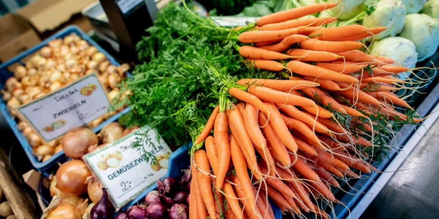 Karotten und Zwiebeln stehen an einem Obst- und Gemüsestand auf einem Wochenmarkt zum Verkauf.
