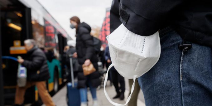 Ein Mann wartet mit einer Maske am Handgelenk auf einen Bus. maske coronavirus
