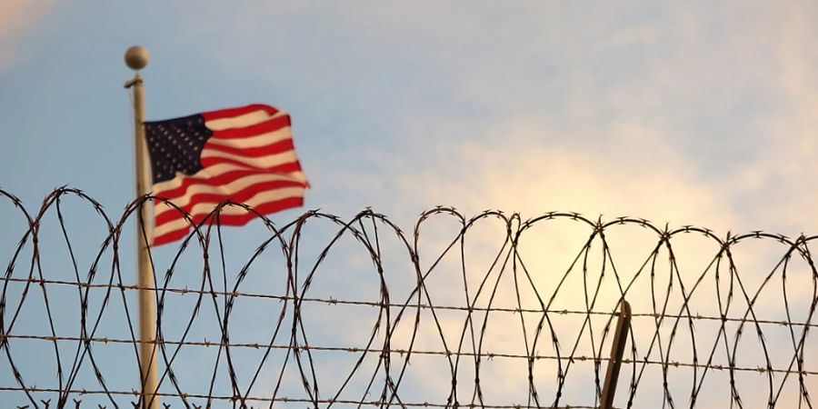 ARCHIV - Eine US-amerikanische Flagge weht hinter einem Stacheldrahtzaun im Wind. Foto: Maren Hennemuth/dpa