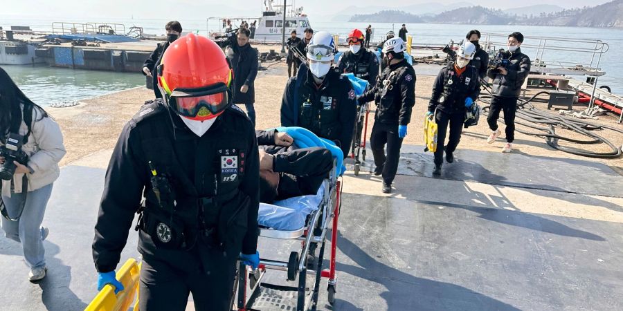 Gerettete Besatzungsmitglieder werden von Rettungskräften auf Bahren getragen, als sie in einem Hafen in Mokpo in Südkorae ankommen.