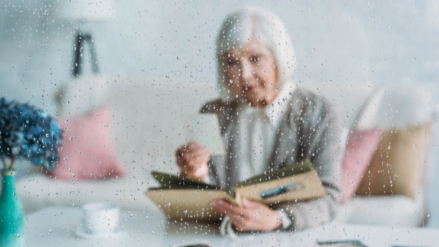 alte frau hinter glasscheibe, regentropfen, schaut foto/ fotoalbum an