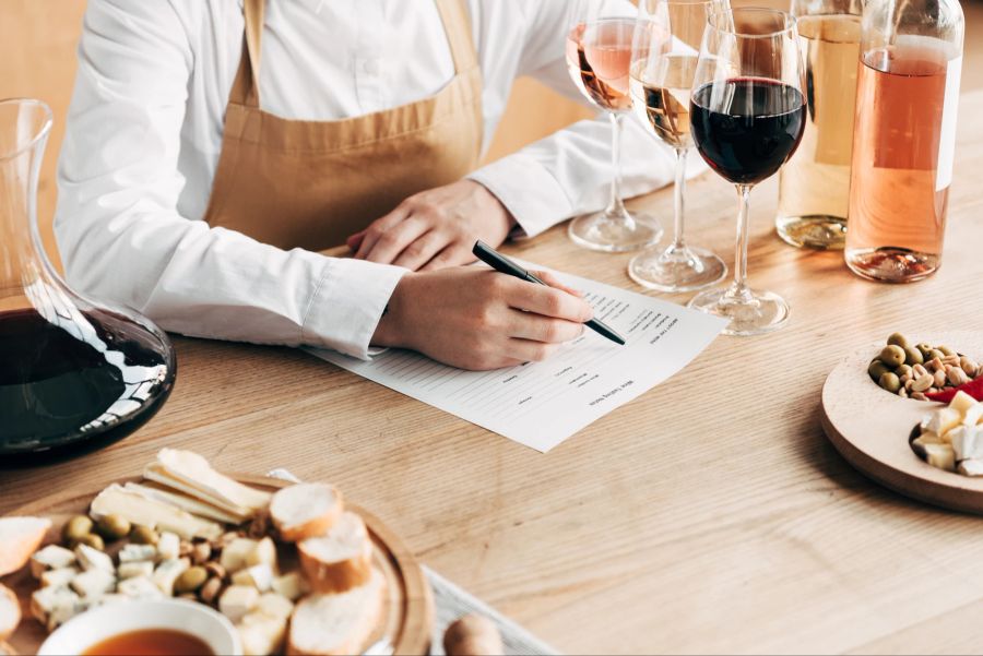 Zugeschnittene Ansicht eines Sommeliers in Schürze, der am Tisch sitzt und in ein Degustationsdokument schreibt