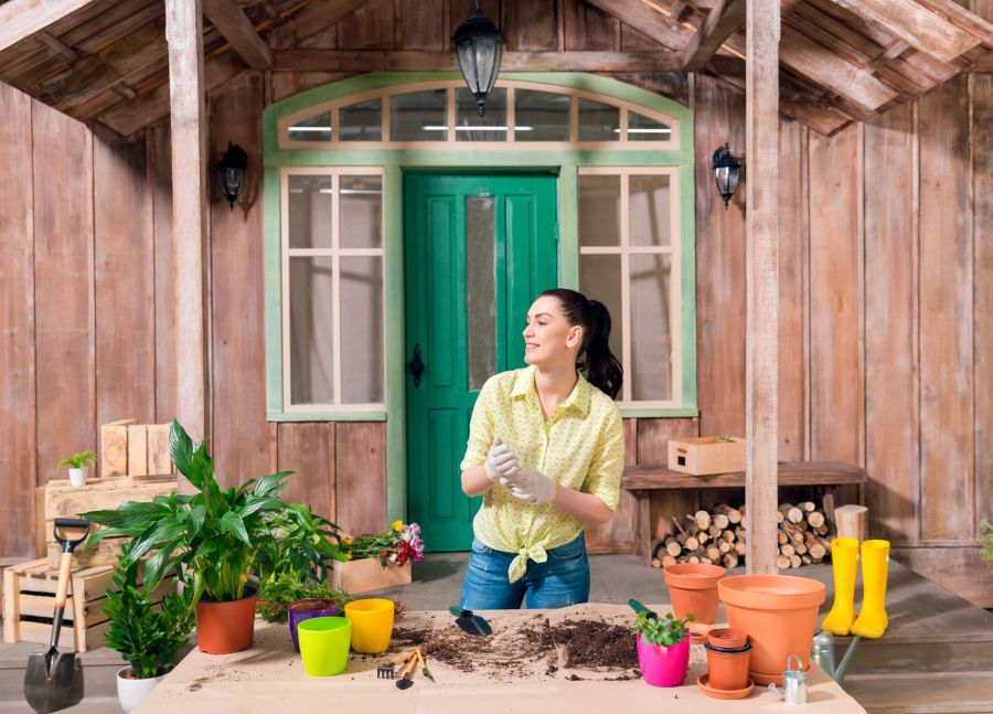 Frau arbeitet mit Pflanzen auf Pflanztisch vor Holzhaus.