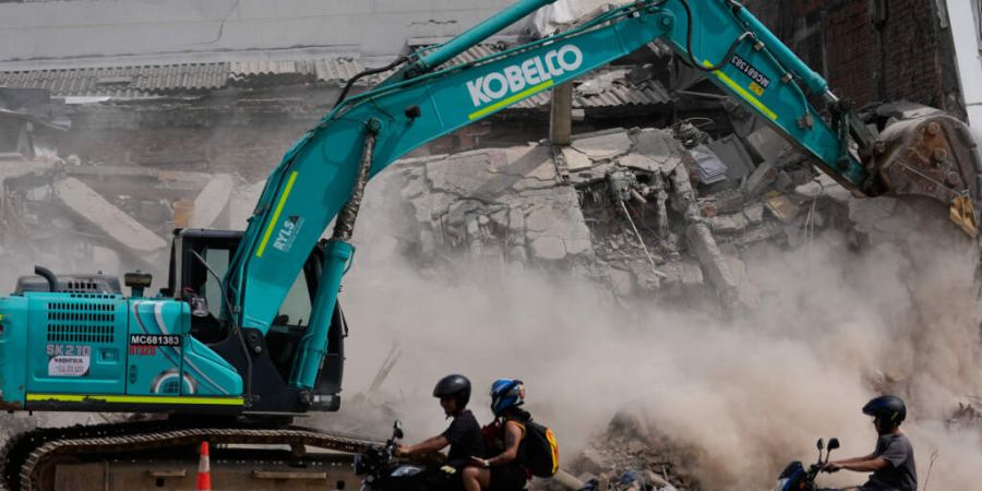 Zwei Tage nach dem Erdbeben fahren Menschen an einem Bagger vorbei, der Trümmer beseitigt. Foto: Fernando Vergara/AP/dpa