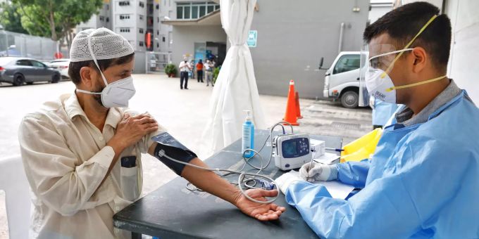 Ein Mann mit Mundschutz bekommt in der Nähe des Wohnkomplexes Toh Guan Dormitory eine Gesundheitskontrolle von einem Arzt. Coronavirus - Singapur