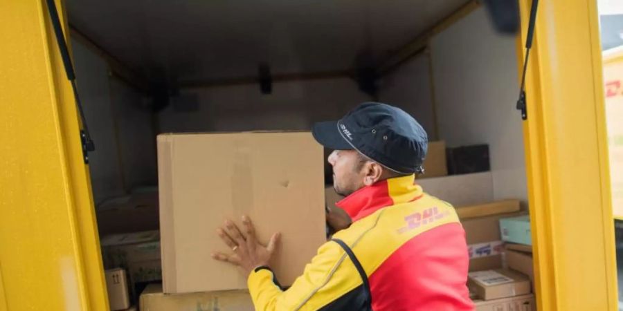 Ein Paketzusteller stellt ein Paket in ein Fahrzeug der Deutschen Post DHL. Foto: Rolf Vennenbernd/dpa