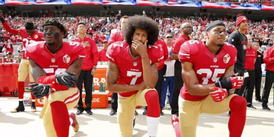 Colin Kaepernick (M.) kniete 2016 mit seinen Teamkollegen Eli Harold (l) und Eric Reid vor einem Spiel der San Francisco 49ers. Foto: John G Mabanglo/EPA/dpa