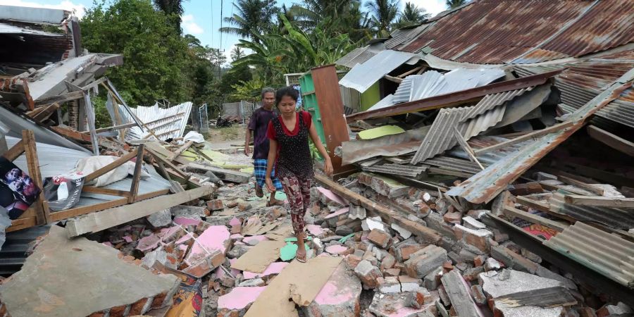 Zwei Bewohner gehen nach dem neuen schweren Erdbeben auf der indonesischen Ferieninsel Lombok durch die Trümmer ihres Dorfes.