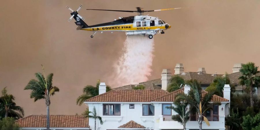 Ein Helikopter versucht mit Wasser ein Feuer bei einer Villa zu löschen.