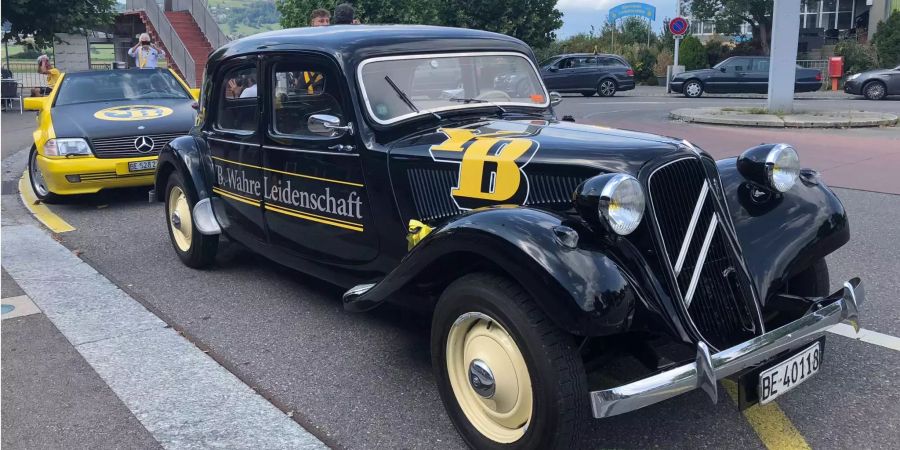 Ein schwarzer Citroen-Oldtimer mit dem Logo von YB, dahinter noch ein zweites YB-Fan-Auto.