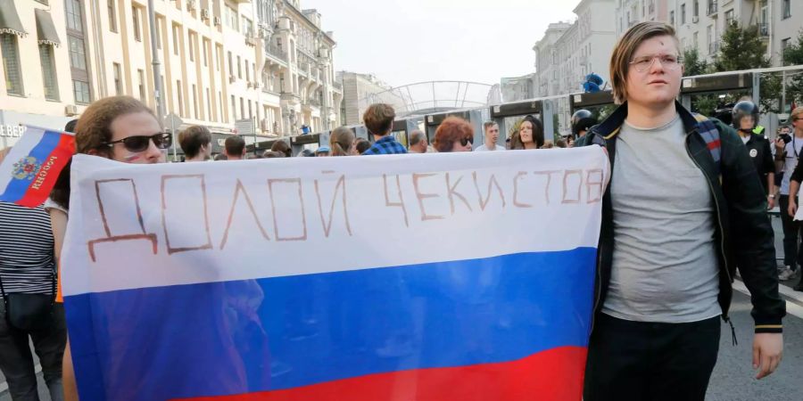 Zwei Demonstranten halten eine russische Flagge mit der Aufschrift «Nieder mit den Tschekisten» hoch.