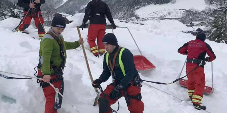 Angeseilte Feuerwehrleute räumen mit Schneeschiebern ein Dach im bayrischen Ramsau. Foto: Tim Oelbermann