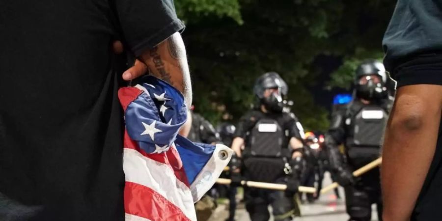 Ein Demonstrant mit einer zusammengeknüllten US-Flagge vor Polizisten: Amerika kommt nicht zur Ruhe. Foto: Allen G. Breed/AP/dpa