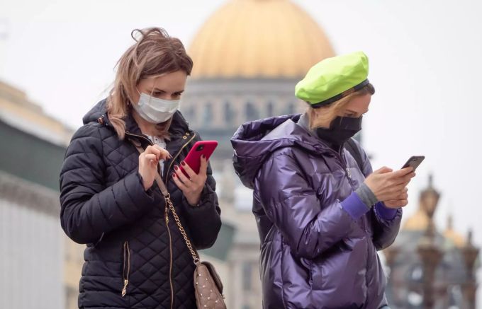 Frauen mit Schutzmasken schauen in der Innenstadt auf ihre Handys. Foto: Dmitri Lovetsky Coronavirus - Russland