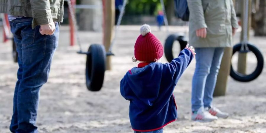 Ein Kind spielt mit seinen Eltern auf einem Spielplatz. Foto: Christoph Soeder/dpa