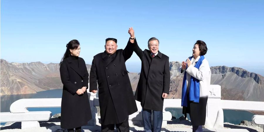 Nordkorea-Machthaber Kim Jong Un und Südkorea-Präsident Moon Jae (Mitte) geben sich die Hand und strecken sie als Zeichen der Zusammengehörigkeit in die Luft.