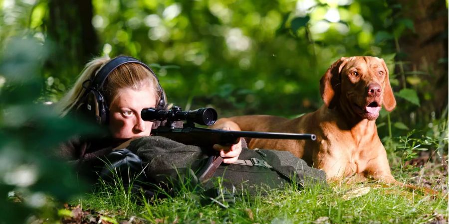 Jägerin Elena Jungk schaut neben ihrer Hündin Lanja durch das Visier ihres Jagdgewehres.