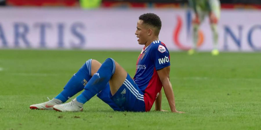 Noah Okafor sitzt nach einem Spiel des FC Basel auf dem Rasen.