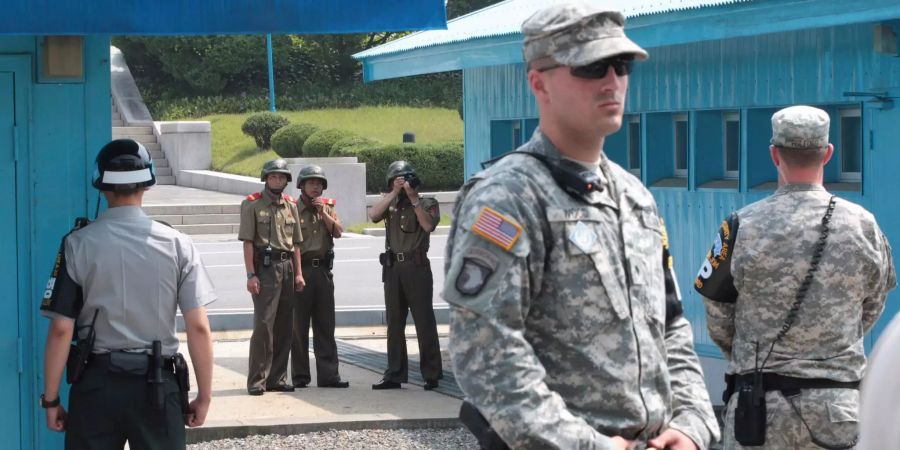 Nordkoreanische Soldaten schauen auf die Südseite der Grenze, während südkoreanische (l.) und US-amerikanische (r.) Soldaten an der entmilitarisierten Zone um Panmunjom (PRK) Wache stehen.