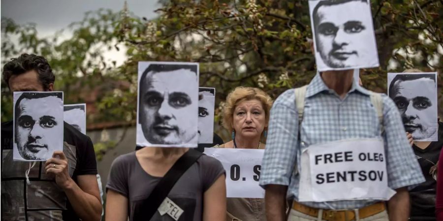 Menschen halten Plakate von Oleg Senzow um gegen seine Inhaftierung zu protestieren.