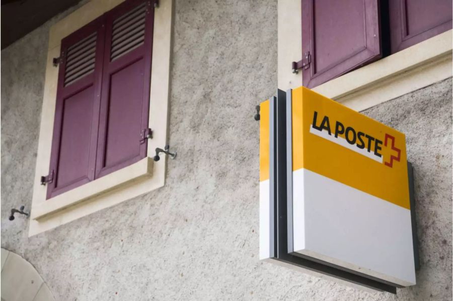Ein altes Gebäude mit weinroten Fensterladen und «La Poste» Schild daran - Keystone