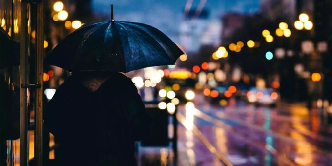Eine Person schützt sich mit einem dunklen Schirm vor dem Regen. Eine Person schützt sich mit einem dunklen Schirm vor dem Regen.