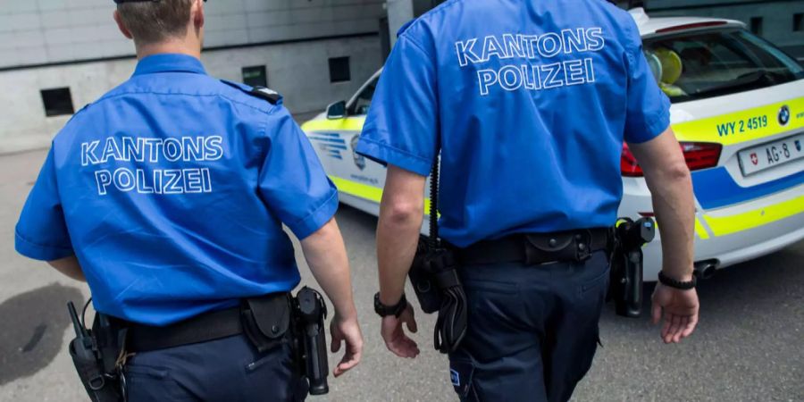 Zwei Polizisten stehen vor einem Fahrzeug der Kantonspolizei Aargau.