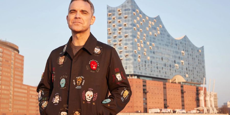 Robbie Williams, britischer Sänger und Songwriter, steht während eines Fototermins auf einer Barkasse im Hamburger Hafen. Im Hintergrund ist die Elbphilharmonie zu sehen.