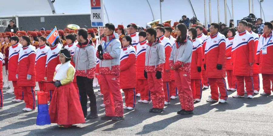 Sportler aus Nordkorea stehen im olympischen Dorf während der Willkommenszeremonie hinter einem Schild mit der Fahne ihres Landes zusammen.