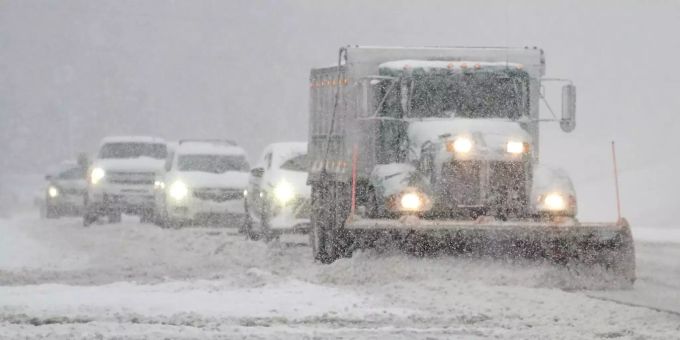 Autos folgen einem Schneepflug auf einer verschneiten Strasse. Schneesturm