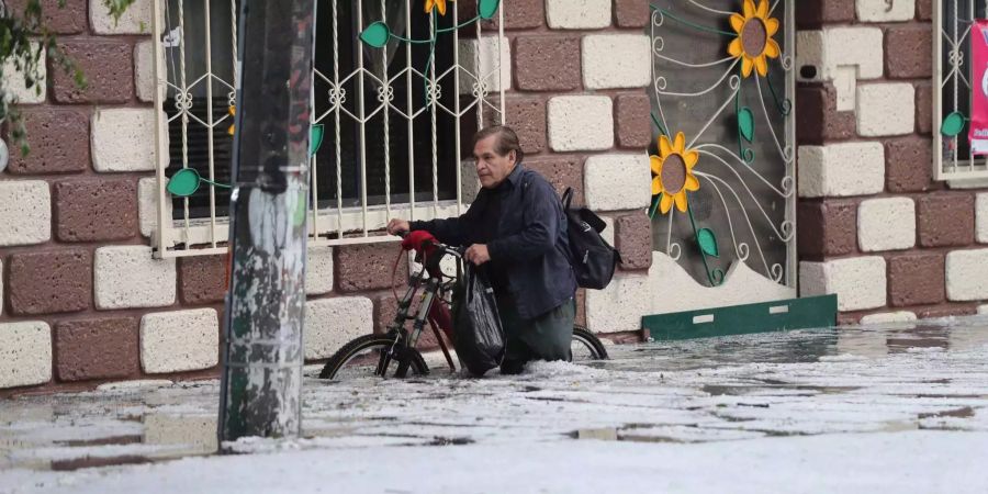 Ein Mann watet mit seinem Fahrrad nach einem Hagelschlag durch eine überschwemmte Strasse.