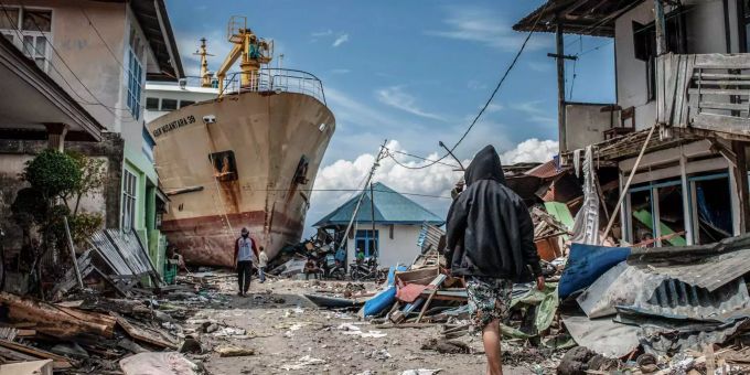 Menschen gehen eine Strasse entlang in der Nähe des Ortes Palu in Indonesien, wo ein Schiff während des Tsunamis an Land gespült wurde. Menschen gehen eine Strasse entlang in der Nähe des Ortes Palu in Indonesien, wo ein Schiff während des Tsunamis an Land gespült wurde.