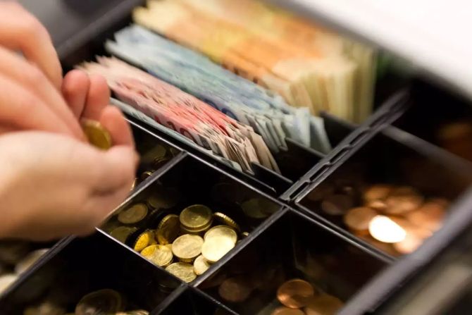 Münzen werden in einem Supermarkt aus der Kasse genommen.