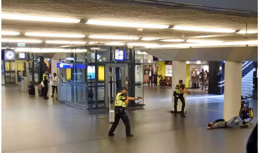 Polizisten richten ihre Waffen auf einen verwundeten 19-jährigen Mann, der von der Polizei angeschossen wurde, nachdem er am Freitag zwei Personen im Hauptbahnhof von Amsterdam, Niederlande, niedergestochen hatte.