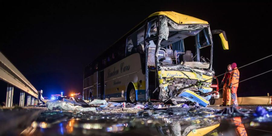 Rettungskräfte stehen auf der Autobahn an einem Unfall vor einem schwer beschädigten Reisebus.