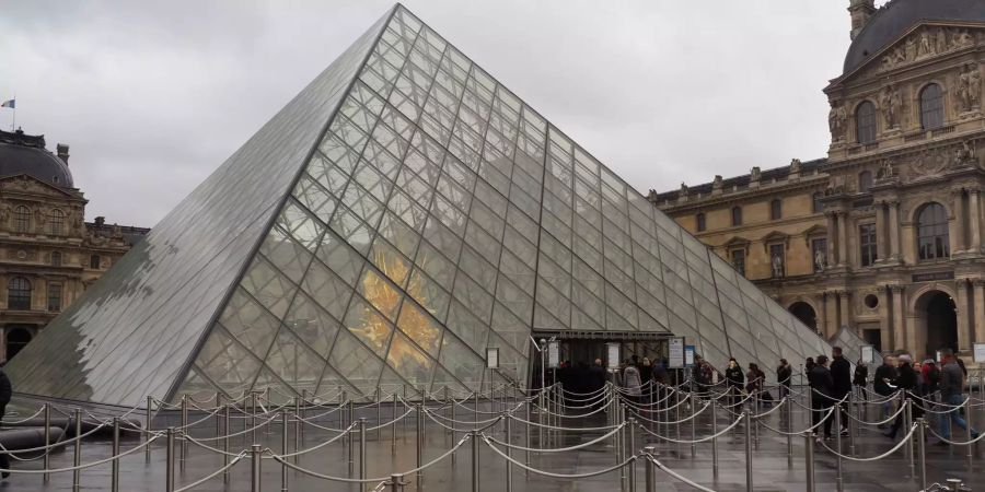 Kaum Besucher stehen vor der Pyramide im Innenhof des Louvre-Museums in Paris.