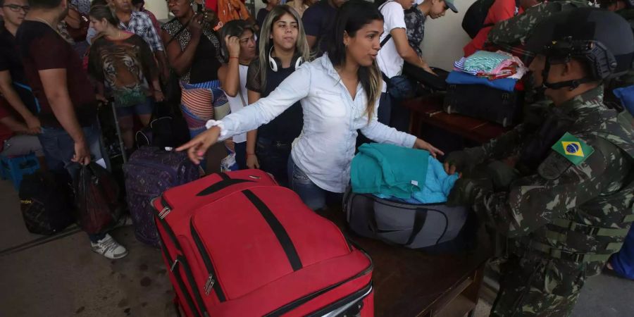 Eine venezolanische Frau spricht zu einem brasilianischen Soldaten. Dieser inspiziert ihr Gepäck am Checkpoint der Grenze von Pacaraima, Brasilien.