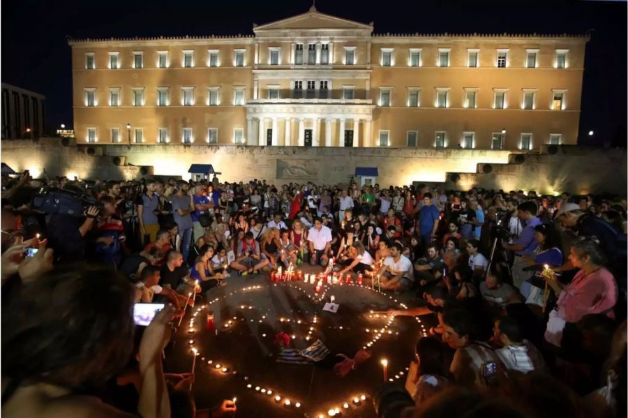 Menschen zünden auf dem Syntagma-Platz in Athen Kerzen für die Brandopfer an.