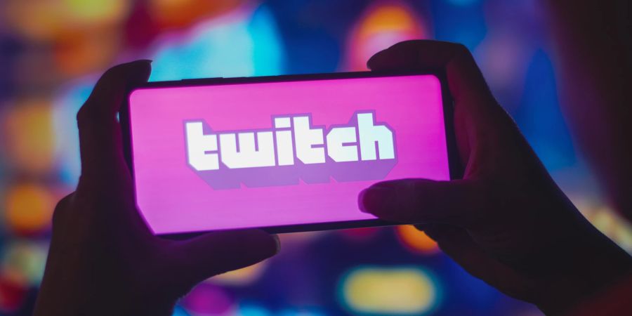 Zwei Hände halten ein Smartphone quer, auf dem Twitch steht