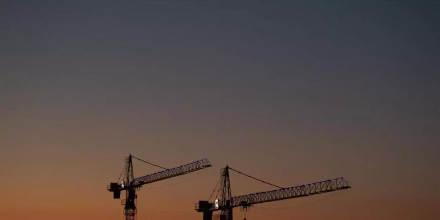 Kräne vor dem Abendhimmel auf einer Baustelle: Die Wirtschaftsstimmung steigt. Foto: Robert Michael/dpa-Zentralbild/dpa