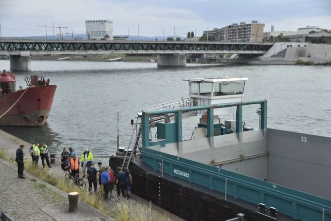 Einsatzkräfte von Polizei und Feuerwehr stehen am Rhein bei dem Frachtschiff- kontrolle brücken
