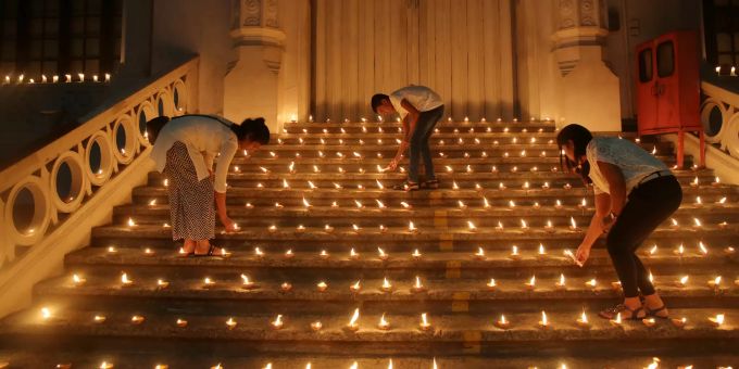 Drei Menschen entzünden Kerzen in Gedenken an die Opfer der Anschläge zu Ostern in Sri Lanka. anschläge ostern sri lanka