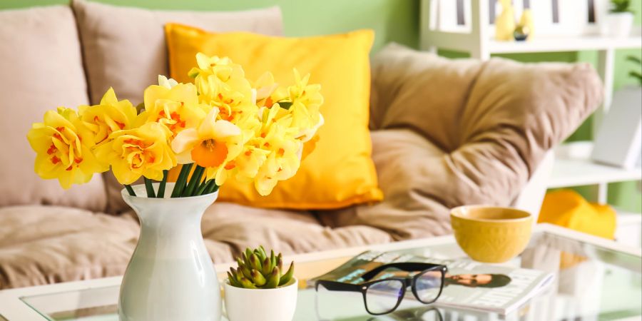 Vase mit Blumen auf Tisch und farbenfrohes Kissen auf Sofa