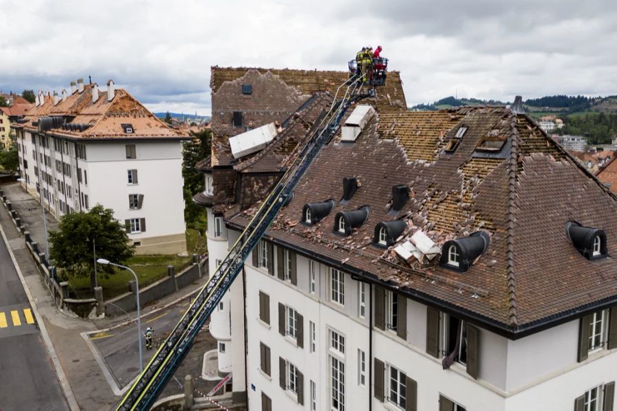 Feuerwehrleute betrachten Schäden an einem Dach, die durch das Unwetter entstanden sind.